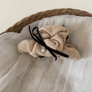 Detail der gestrickten Haarklammer mit beigem Garn, schwarzer Schleife und Perlenanhänger