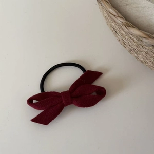 Detail of burgundy wool-like bow hair tie with elastic band on minimalist background