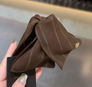 Détail d'une pince à cheveux en tissu rayé marron avec bouton décoratif en métal doré gravé