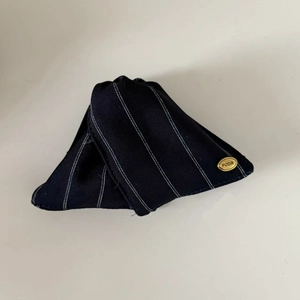 Détail d'une pince à cheveux en tissu rayé avec étiquette métallique dorée et texture sergé