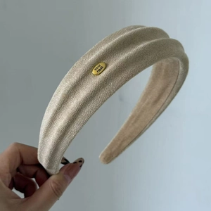 Detail eines beige strukturierten Haarreifens mit goldenem ovalen Handarbeitsschild