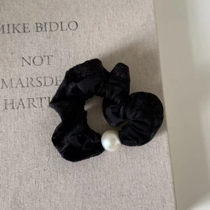 Close-up of elegant velvet scrunchie with large pearl detail on textured background