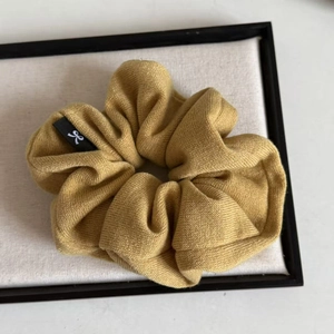Detail of mustard yellow ribbed knit scrunchie with a small bow logo label
