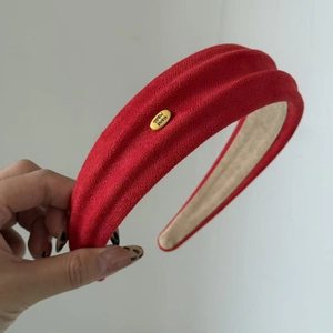 Detail eines roten breiten Stirnbands mit goldenem Hand Made Metallschild und Wildleder