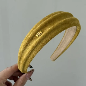 Detail des goldgelben Samt-Stirnbands mit plissierter Textur und handgefertigtem Emblem
