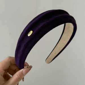 Nahaufnahme des lila Samtstirnbands mit handgefertigtem goldenem Metallemblem