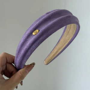 Detailaufnahme des violetten Wildleder-Haarreifens mit goldenem Hand Made Metall-Logo