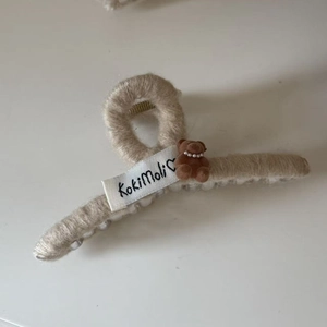 Close-up of a cute plush bear hair claw clip with pearls and warm beige knitted texture