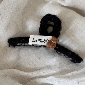 Detail of plush black shark hair claw clip with a cute brown bear and white woven label