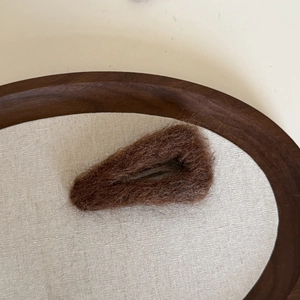 Gros plan d'une pince à cheveux en peluche marron sur un plateau rétro en lin