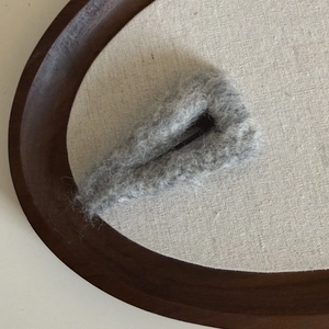 Détail d'une pince à cheveux triangulaire en peluche grise sur lin et plateau bois