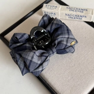 Detail of navy blue plaid bow hair claw clip with a gold metal plate on grey texture