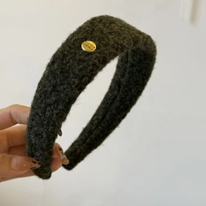 Détail du serre-tête en polaire vert olive avec un badge métallique doré gravé