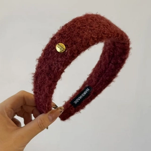 Détail d'un serre-tête en peluche bordeaux avec logo doré et étiquette fait main