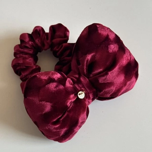 Makroaufnahme des burgunderroten Samt-Scrunchies mit Schleife und Gold-Anhänger