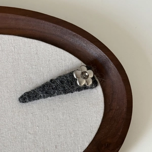 Minimalist silver flower hair clip with grey wool felt on a decorative wooden tray
