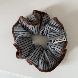 Macro detail of grey striped hair scrunchie with brown velvet trim and brand label