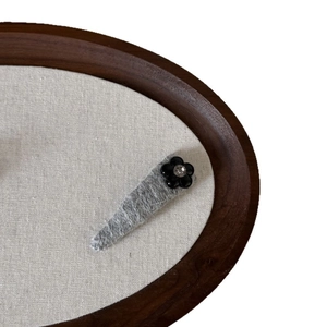 Minimalist grey tweed hair clip with a black flower and crystal accent on wooden tray