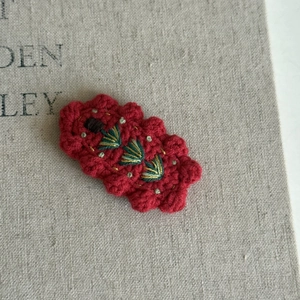 Detail of handmade crochet hair clip with green and gold floral embroidery on red base