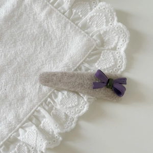 Detailed macro view of cream wool hair clip with a soft purple bow on lace fabric