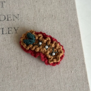 Close-up of a handmade crochet Christmas hair clip with red yarn and pearl accents