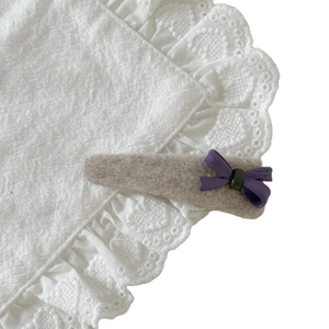 Creamy white wool hair clip with a purple bow accent on an elegant lace background