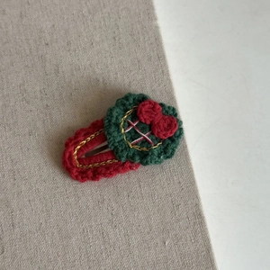 Detail of handmade crochet Christmas wreath hair clip with festive red bow and gold thread