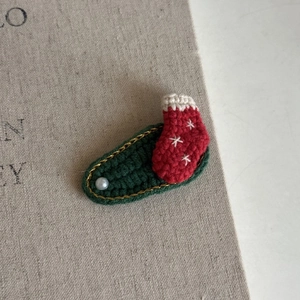 Close-up of handmade crochet Christmas sock hair clip with pearl and gold thread details