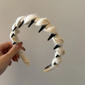 Detail of a beige knitted headband featuring black punk style conical spikes and texture