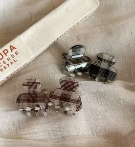 Detail view of plaid mini hair claws in black and brown patterns on beige fabric background