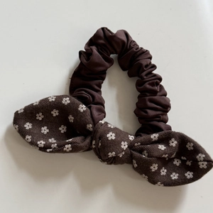 Dettaglio di uno scrunchie marrone con fiocco a fiori e pois bianchi per capelli