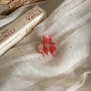Macro detail of a red plaid checkered hair claw clip on soft textured linen fabric