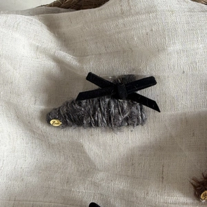 Close-up of velvet bow hair clip with plush grey fabric and golden Love pendant