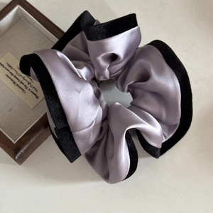 Elegant lilac satin scrunchie with black velvet trim next to a wooden jewelry box