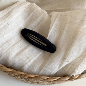 Minimalist black velvet teardrop hair clip on a natural woven linen background