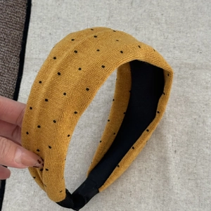 Detail eines senfgelben Strickstirnbandes mit schwarzen Punkten und Faltendesign