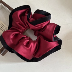 Detailed close-up of wine red satin scrunchie with elegant black velvet piping trim