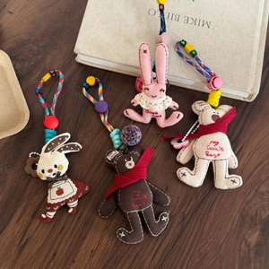 Handmade pink lace bunny and embroidered bear plush keychains on a rustic wood background
