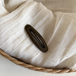 Detailed view of brown oval hair clip with matte velvet texture on a woven fabric base
