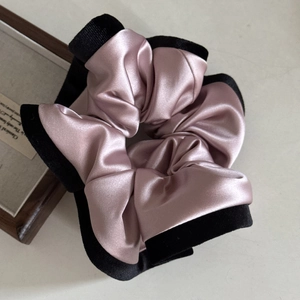 Detailed close-up of champagne satin scrunchie with thick black border on a cream base