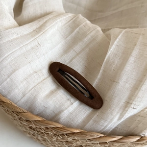 Detail shot of a dark brown matte Fair Isle style BB hair clip on textured beige fabric