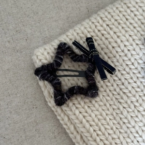 Detail view of plush black star hair clip and navy blue bow on white knit fabric