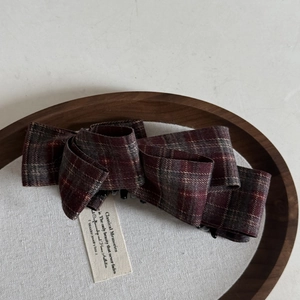 Close-up of a vintage red plaid bow banana hair clip on a minimalist wooden tray