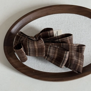 Detailed close-up of brown plaid fabric hair bow clip showing knitting texture on wooden tray