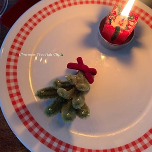 Handmade green plush Christmas tree hair clip with red bow and gold beads on a plate