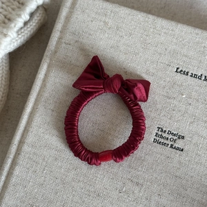 Dettaglio dell'elastico per capelli in raso rosso vino con fiocco su sfondo di libro antico