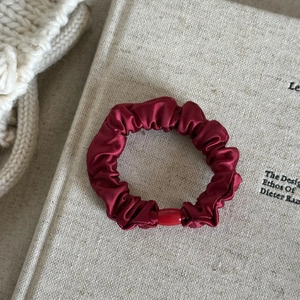 Dettaglio di un elastico in raso bordeaux con una perla su uno sfondo di tessuto morbido