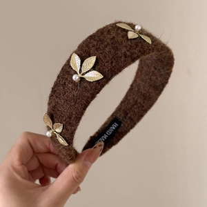 Detail of brown faux shearling headband with golden leaf accents and pearl beadings