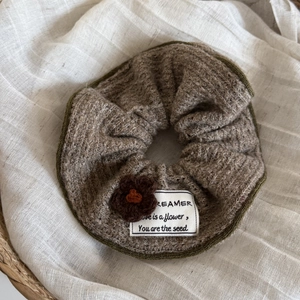 Detail of knitted coffee scrunchie with olive trim, crochet flower, and fabric label