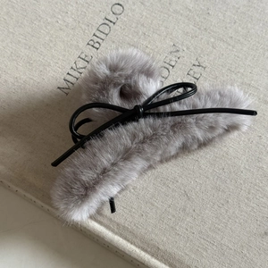 Détail macro d'une pince à cheveux en peluche grise avec un délicat nœud en cuir noir